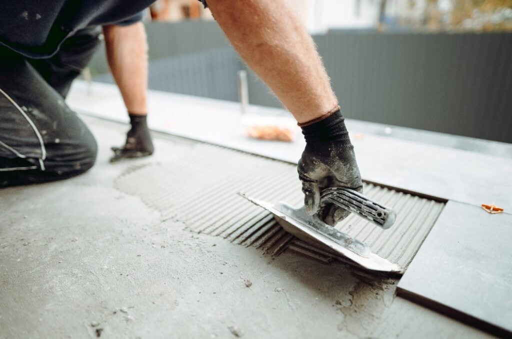 Bodenbelag und Fliesenlegen. Hand eines professionellen Fliesenlegers beim Verlegen von Bodenfliesen auf einer Klebefläche auf dem Balkon